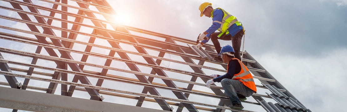 Two male construction workers on a steel frame, with the sun  and party cloudy skies in the background
